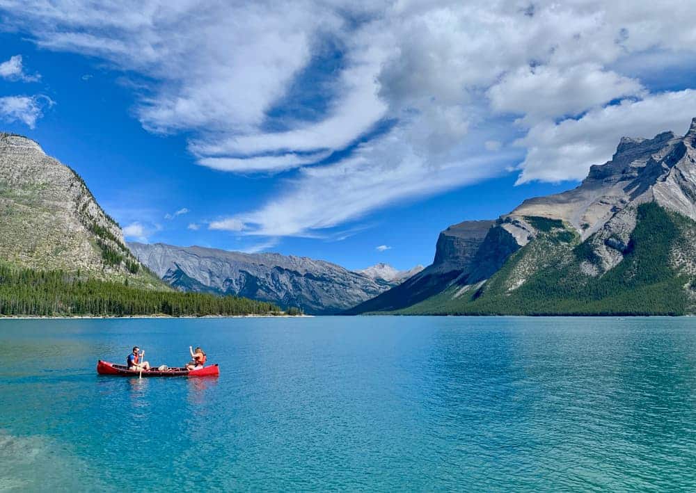 Visitors in Banff National Park enjoy paddling in a canoe on a serene lake, with breathtaking mountains forming a majestic backdrop.