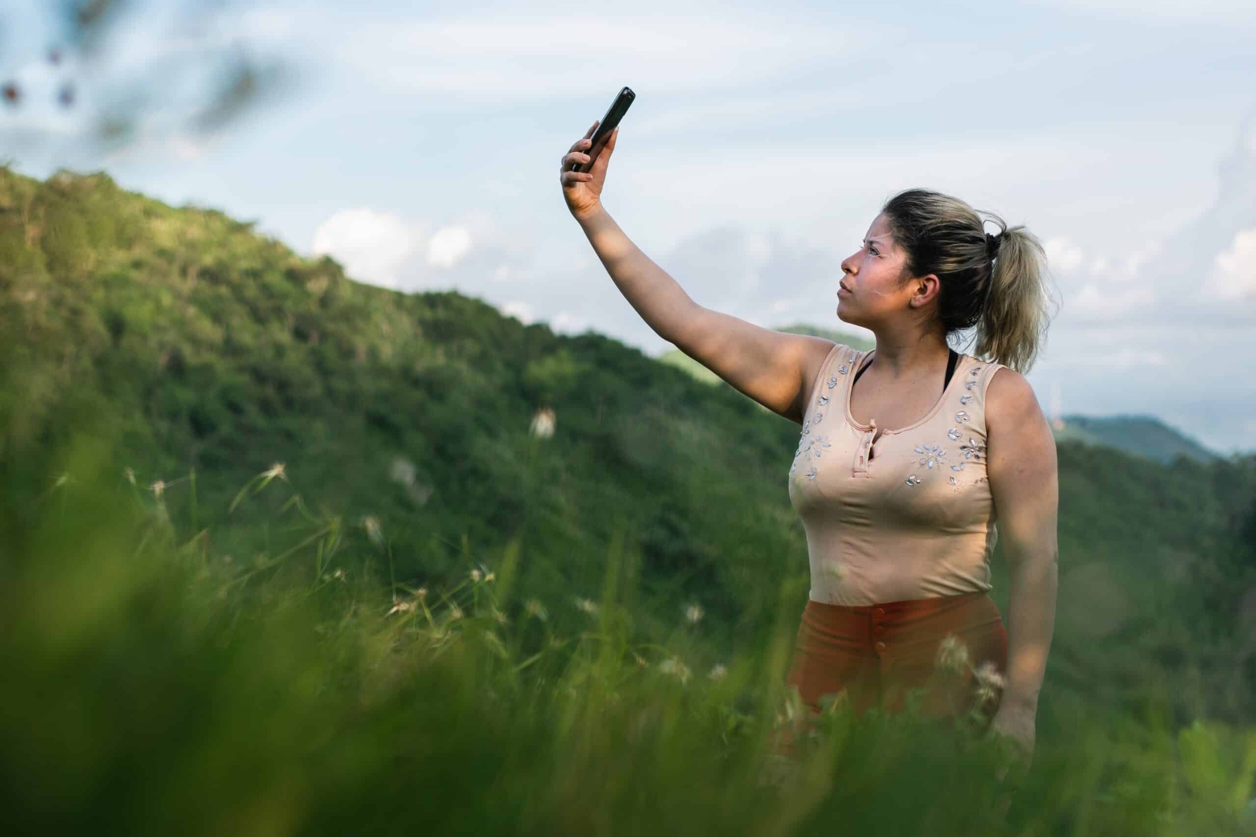 A woman taking a selfie in a grassy field while enjoying improved signal coverage for satellite-to-cell service.