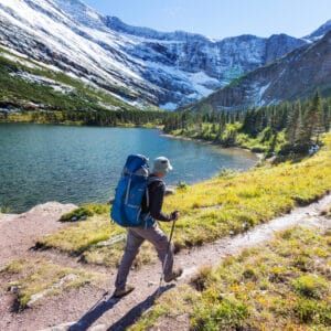 A hiker walking along a trail near a lake in Glacier National Park.