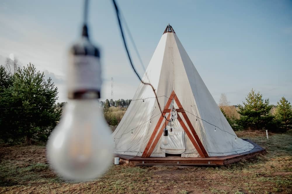 A teepee tent with a glamp aesthetic, safely featuring a light bulb hanging from it.