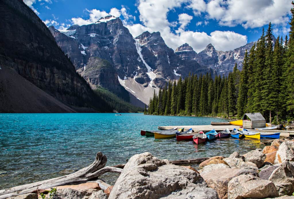Canoes on the shore of a lake in Banff National Park, with mountains in the background during camping season.