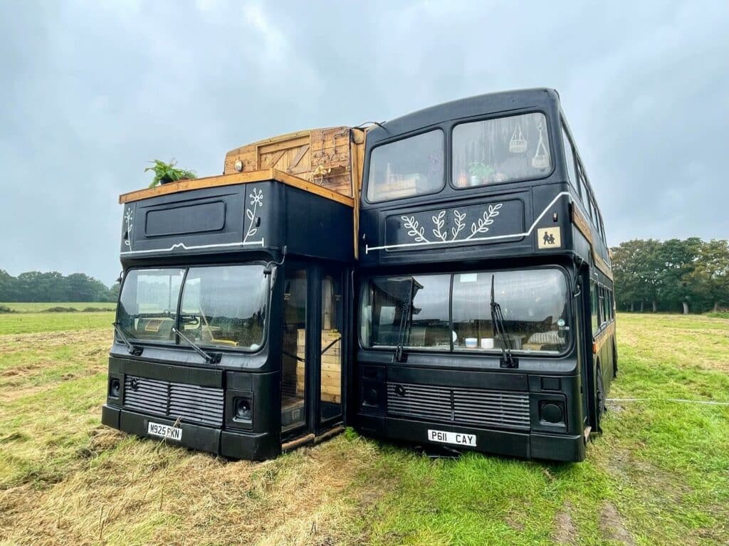 Two double-decker buses converted into Sustainable Glamping Pods parked in a field at Wolds Farm Stay.