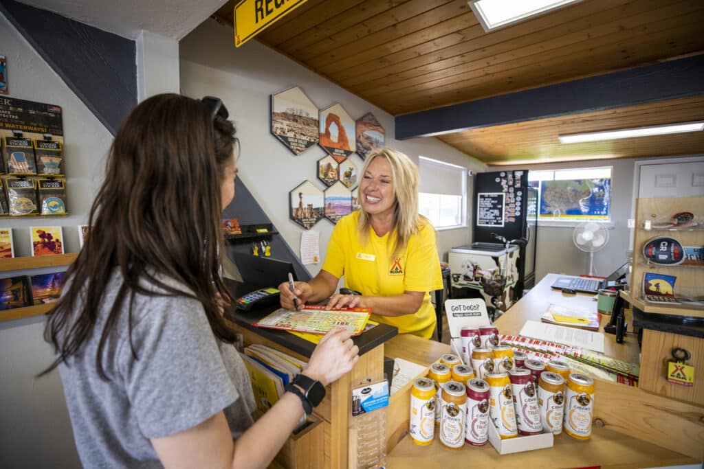 A woman in a yellow shirt is standing at the counter of KCN Campgrounds, an outdoor hospitality industry store.