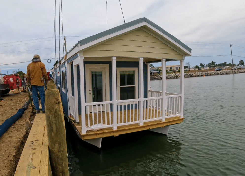 A man is standing next to a Innovative Bungalow Boat on a dock.