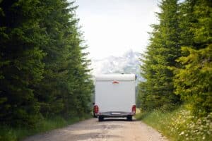 A white truck driving down a dirt road in a forest, surrounded by the serene beauty of nature.