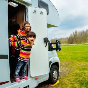 Two children standing out of the door of an RV in a Sun Communities vacation park.