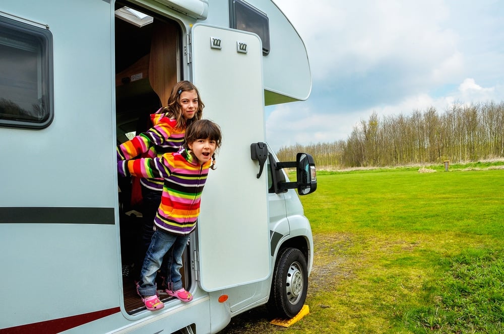 Two children standing out of the door of an RV in a Sun Communities vacation park.