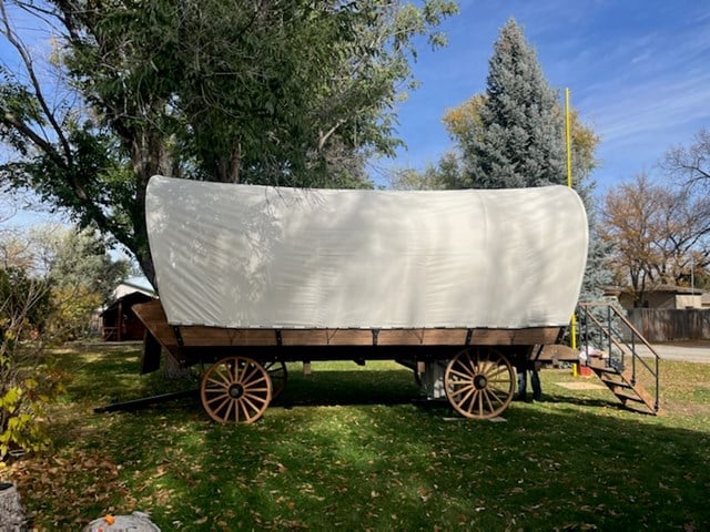 A covered wagon is parked in a grassy area at KCN Campgrounds.