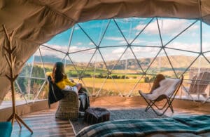 A woman is sitting in an igloo with a view of the mountains at the Glamping Show Americas 2023.