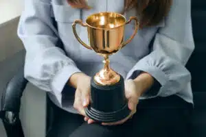 A woman holding a gold trophy in an office chair, representing her success as a leading franchise owner in the recession-proof KOA franchise.
