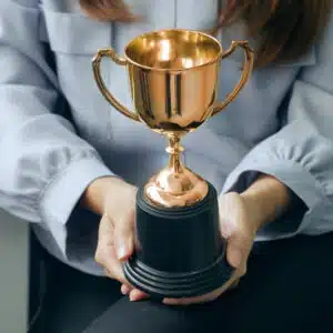 A woman holding a gold trophy in an office chair, representing her success as a leading franchise owner in the recession-proof KOA franchise.