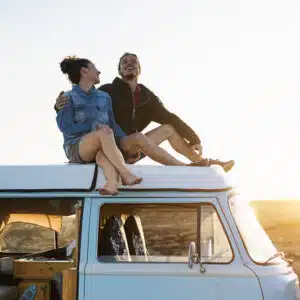 Couple enjoying camping season on top of a van at sunset.
