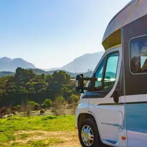 A blue and white RV parked in a field with mountains in the background, showcasing the growth of the Spanish caravanning sector.