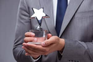 A businessman proudly holding an award with a star on it, representing his recognition as the Best Employer in the Manufacturing industry at Grand Design RV.