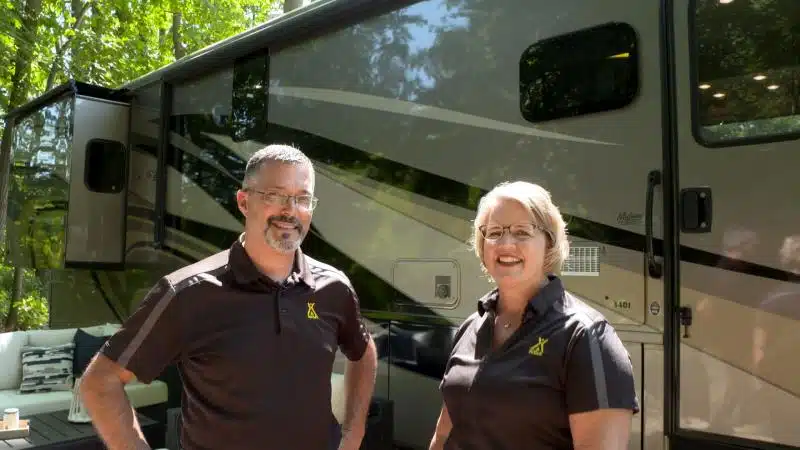 A couple standing in front of an RV at the KOA Campground in Michigan.