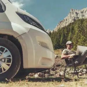 A man sitting in front of a van with a laptop, exploring virtual tours.