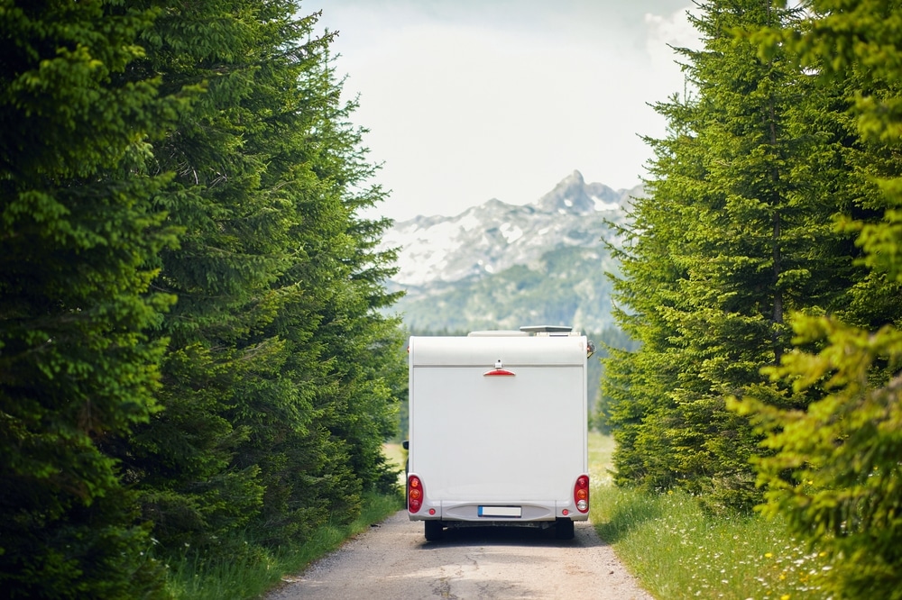 A white rv is driving down a dirt road in a forest.