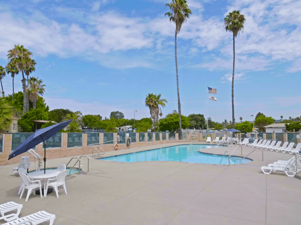 Mission Bay RV Resort features an expansive swimming pool area adorned with lounge chairs and palm trees, perfect for relaxation and enjoying the sun.