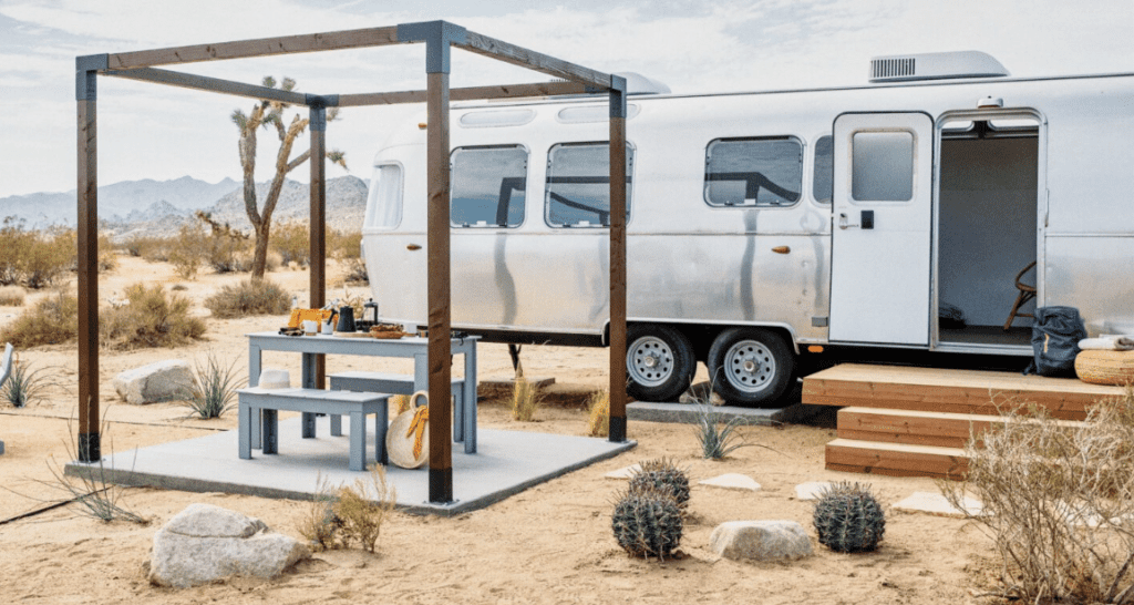 A luxurious glamping experience in the desert, complete with an airstream, table, and chairs.