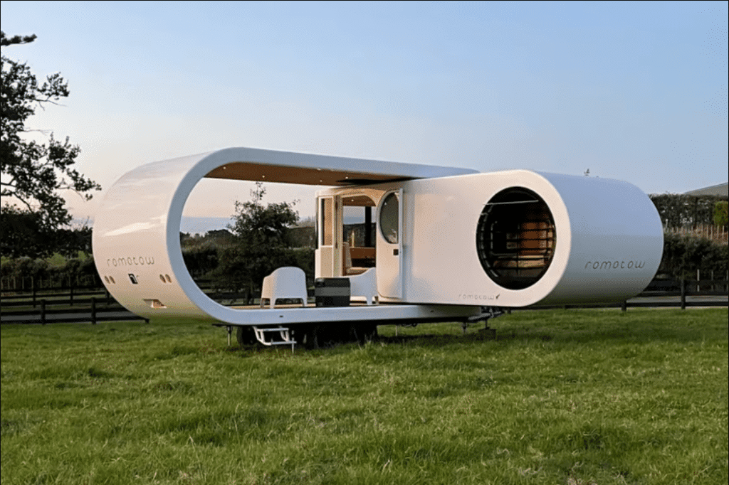 An affordable small white house in the middle of a field with a swinging RV nearby.