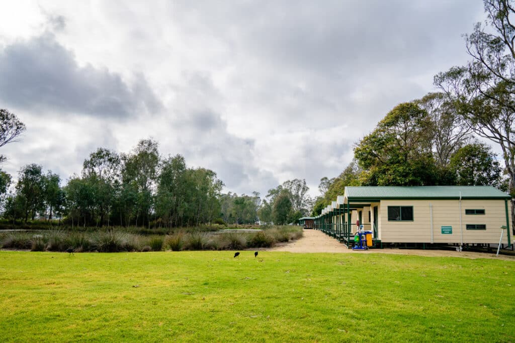 A group of cabins on a grassy area near a pond, perfect for RVing and camping at Victoria Lake holiday park.