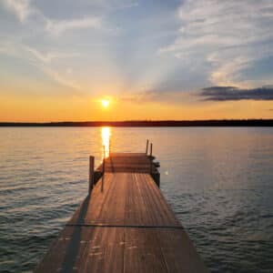 A dock on a lake in Duck Mountain Provincial Park with the sun setting behind it, offering an idyllic spot for outdoor recreation in two provinces.