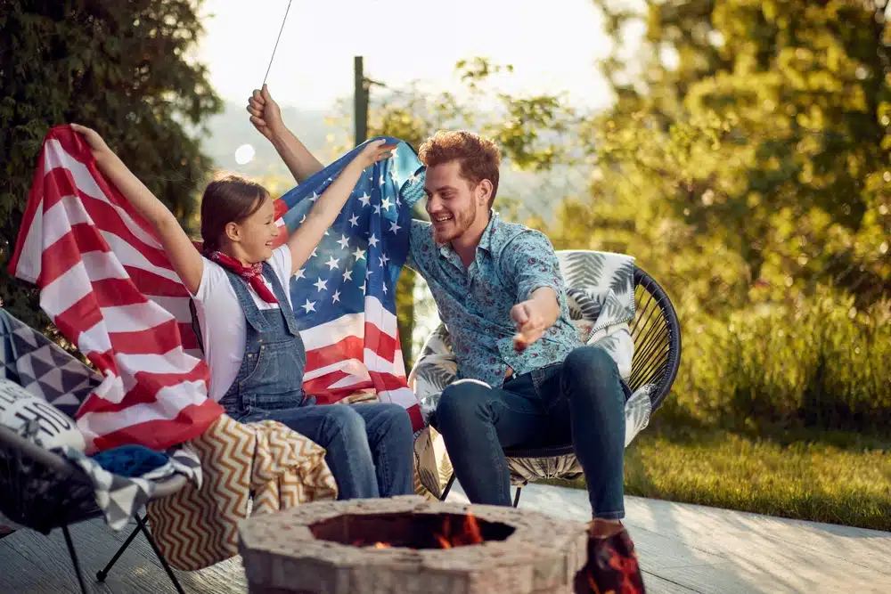 A man and a woman sitting around a fire pit with an American flag, highlighting the Double-Digit registration growth seen in KOA records.