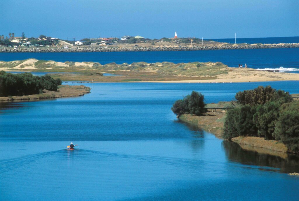 Explore Western Australia's beautiful BIG4+Dongara Denison Beach Holiday Park, where a boat is floating down a river near a beach.