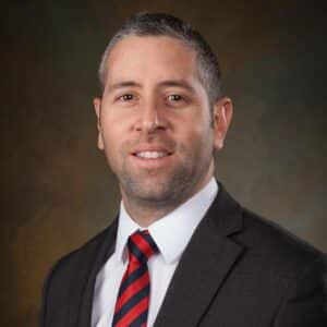 A man in a suit and tie is posing for a photo during the MC Fireside Chats event happening on August 23rd, 2023.