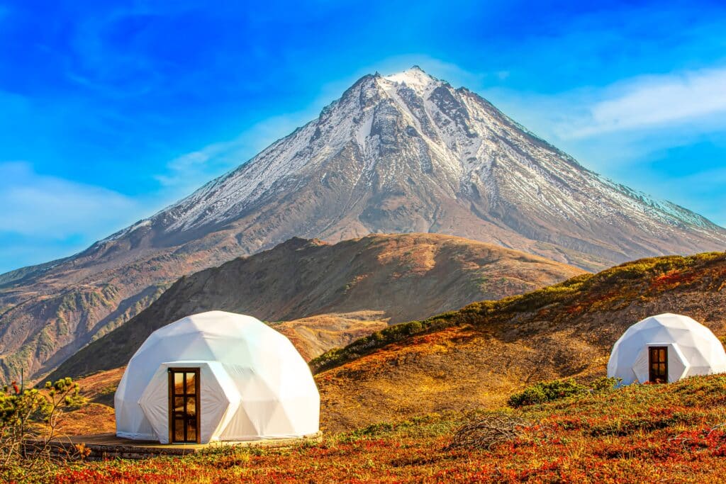 Two white tents set up in front of a stunning mountain, creating an idyllic glamping experience amidst the outdoors.