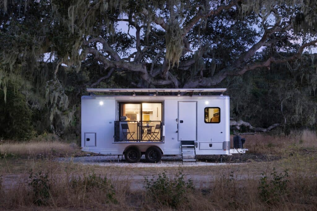 A tiny house with a Living Vehicle parked in the midst of an off-grid oasis, featuring a serene tree in the background.