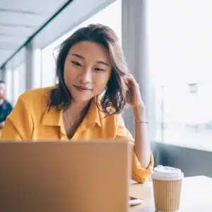 A young asian woman participating in a webinar about Texas Legislation while using a laptop in a cafe.