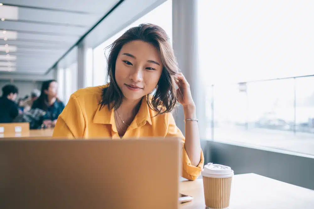 A young asian woman participating in a webinar about Texas Legislation while using a laptop in a cafe.