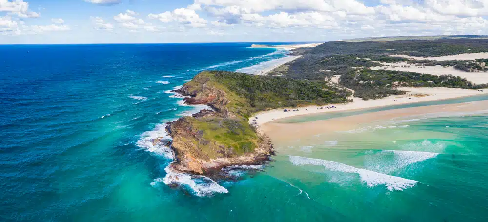 An aerial view of a beach and ocean on the Fraser Coast with modern booking systems available at nearby caravan parks.