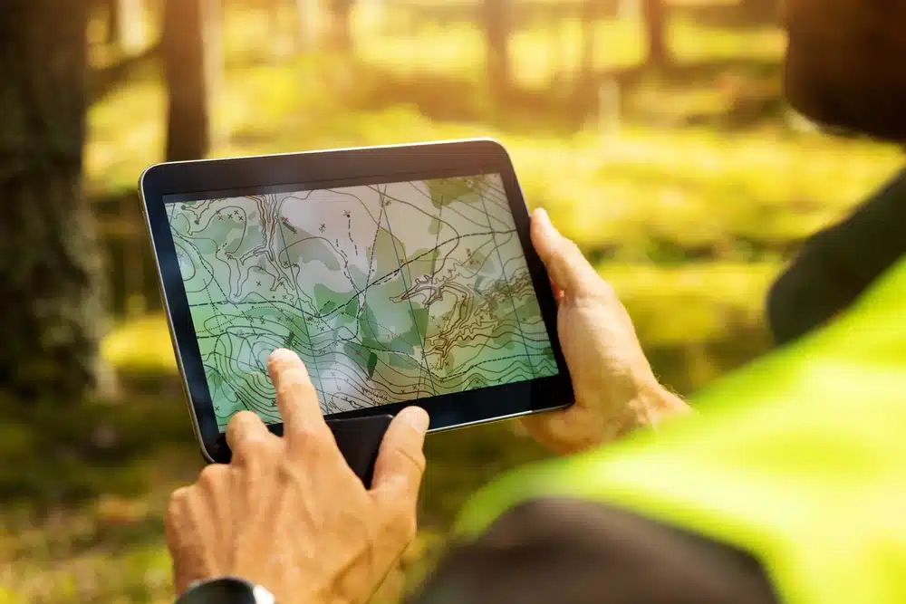 A man is holding a tablet with a map of a forest for a Glamping Resort Development.