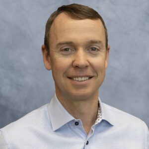 A man in a blue shirt smiling for the camera at MC Fireside Chats on October 25th.
