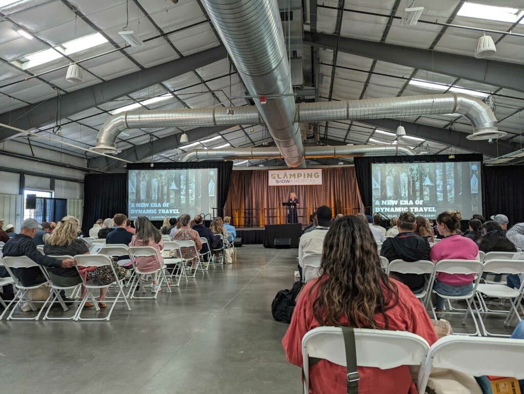 At the Glamping Show Americas 2023, a group of people gather in chairs within a large room to discuss Global Travel Trends.