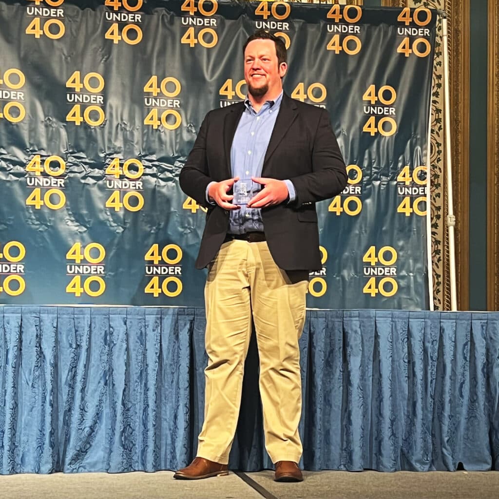 A man standing on stage holding an award for being a 40 Under 40 Star.