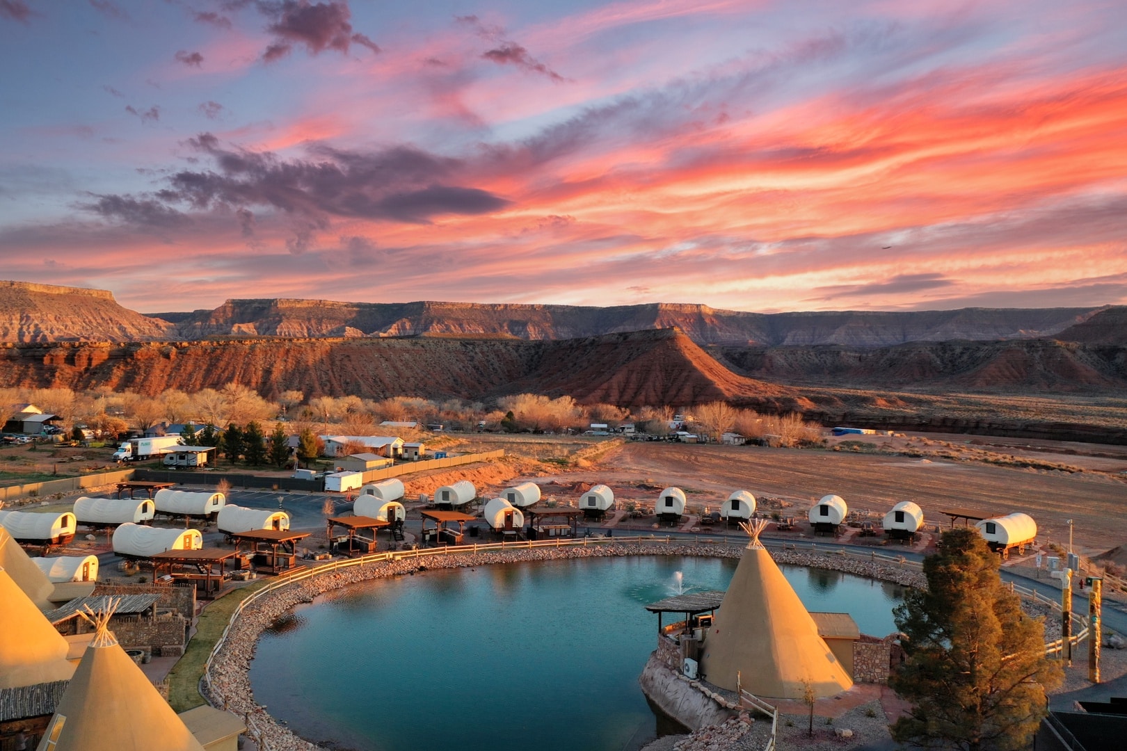 A sunset over a pond with tents and teepees.