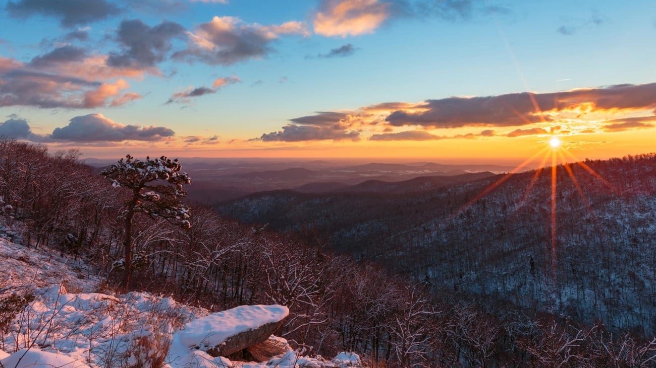 The sun is setting over a snow covered mountain in Shenandoah National Park.