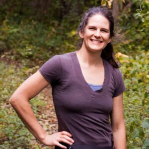 A woman standing in the woods with a smile on her face, photographed on February 14th, 2024.