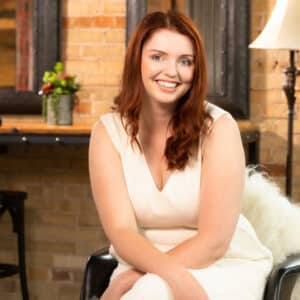 A woman in a white dress sitting on a chair during the MC Fireside Chats on February 14th, 2024.