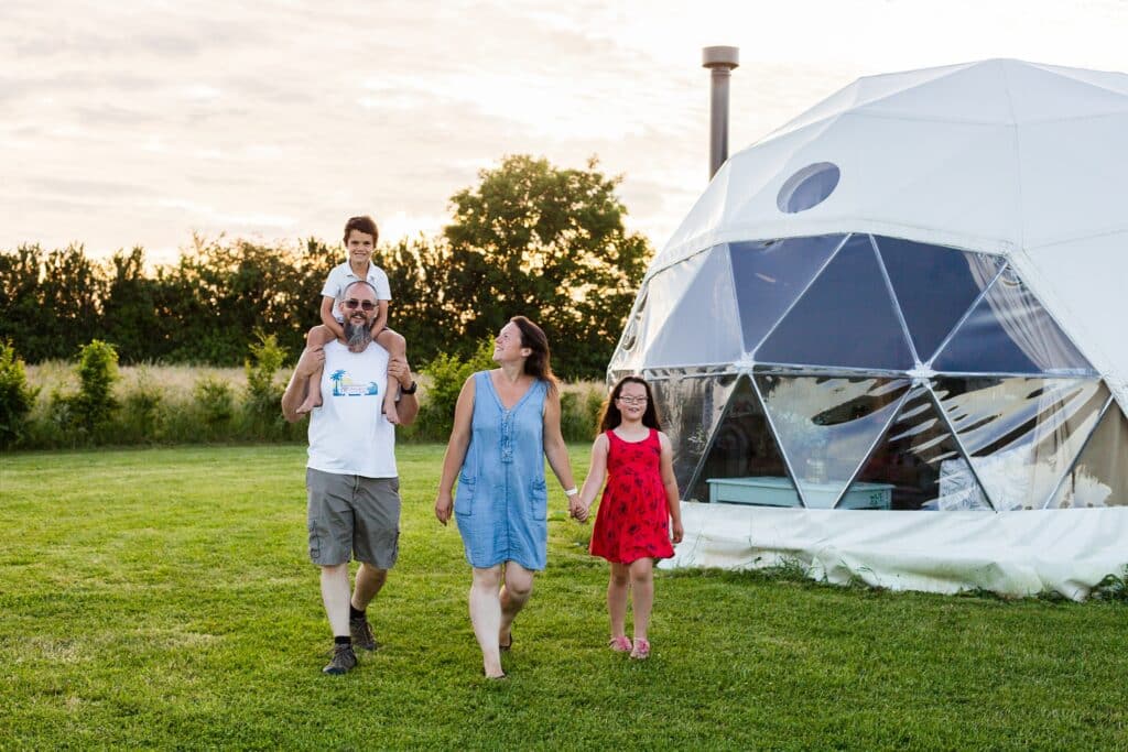 A family is walking in front of a white igloo tent at Somerset Glamping.