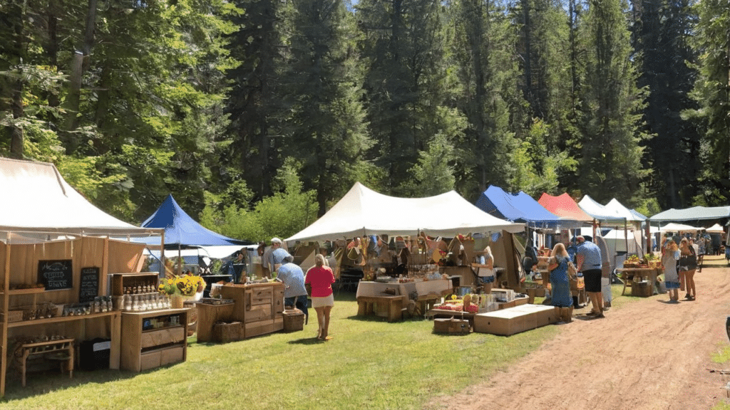 A group of people at a farmers market in a wooded area, celebrating the event success of local businesses.