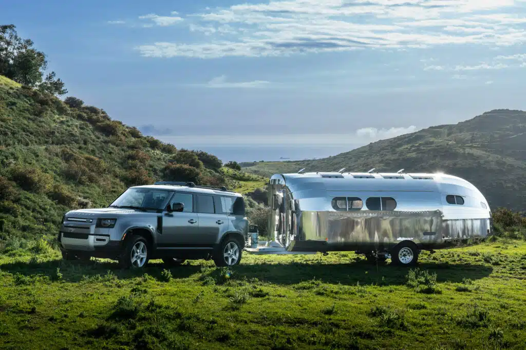 A silver land rover is parked next to a Bowlus Rivet travel trailer.