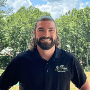 Man with a beard smiling outdoors wearing a black polo shirt with "broad river campground" logo, captured on March 20th.