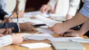 A business meeting in progress with a closeup of participants' hands exchanging auto draft documents over a table.