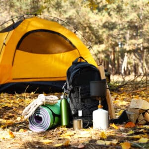 A camping setup in Inyo National Forest with a yellow tent, surrounded by fallen leaves, featuring backpack, rope, firewood, and camping gear.