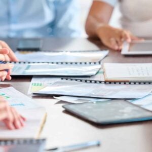 Close-up of hands of business professionals working with auto draft documents and digital devices during a meeting at a conference table.