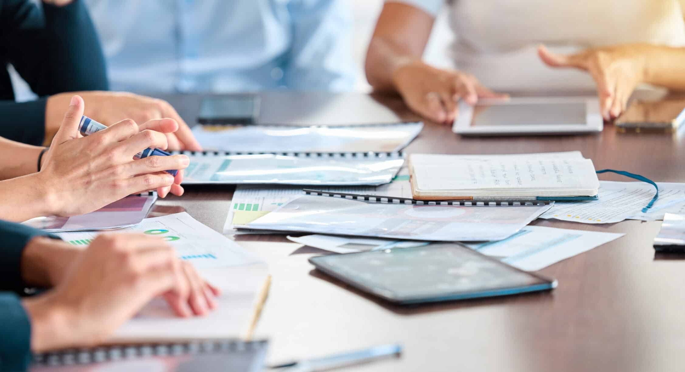 Close-up of hands of business professionals working with auto draft documents and digital devices during a meeting at a conference table.